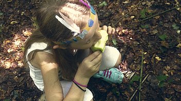 Bild: Mädchen isst Apfel auf Waldboden