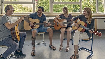 Bild: Eine fröhliche Gruppe erlernt gemeinsam das Gitarrenspielen