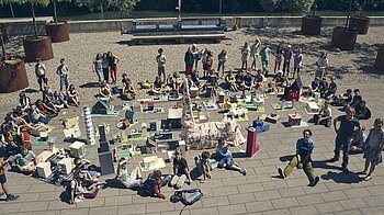 Bild: Kinder sitzen mit ihren selbstgebauten Häusern auf den Platten vor dem kontiki in der Sonne.