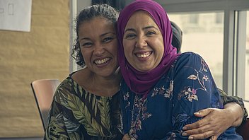 Bild: Zwei lachende Teilnehmerinnen von Frau und Beruf international – mit und ohne Kopftuch