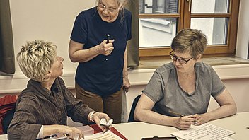Bild: Zwei Frauen und eine Dozentin während des Erlernens von Kalligrafie