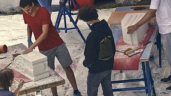 Bild: Junge Leute beim Steinbildhauen mit Ytongklötzen im freien