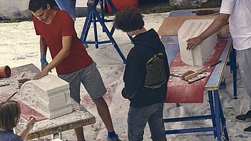 Bild: Junge Leute beim Steinbildhauen mit Ytongklötzen im freien