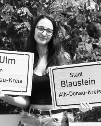 Bild: Frau hält Stadtschild Blaustein  und Schild vh Ulm im Alb-Donau-Kreis