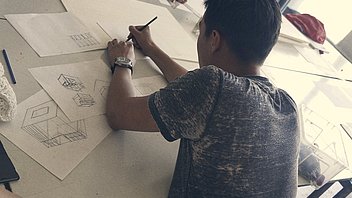 Bild: Junge skizziert im Atelier auf Tisch Architektur-Entwürfe
