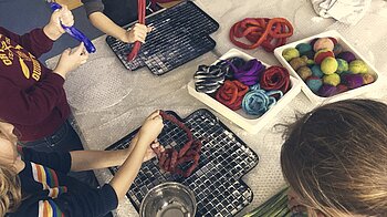 Bild: Filzende Kinder mit Gummimatten auf Tisch und Wollknäuel