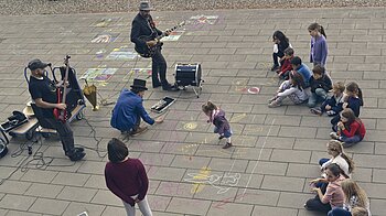 Bild: Kinder sitzen vor Musikband und malen auf dem Pflaster vor dem kontiki