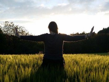 Frau steht mit ausgestreckten Armen in Richtung Sonne